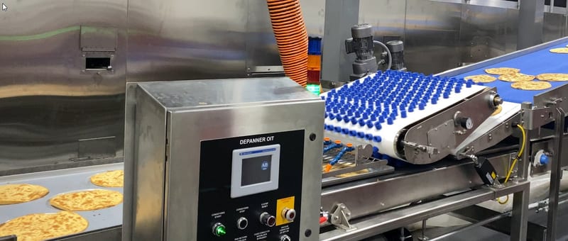 Vacuum depanner above pizza crusts on a blue conveyor